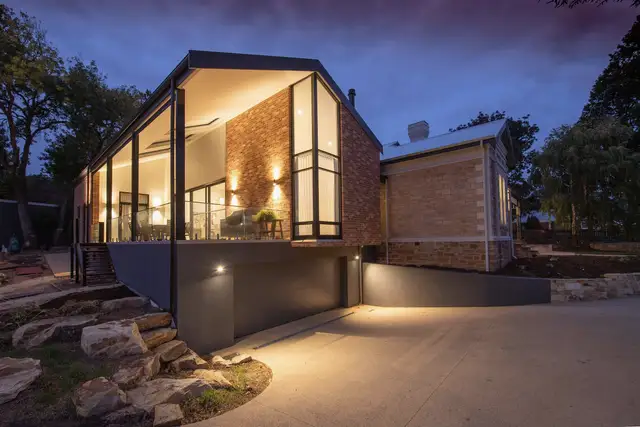 Gabled addition with tall lit windows above a garage at twilight