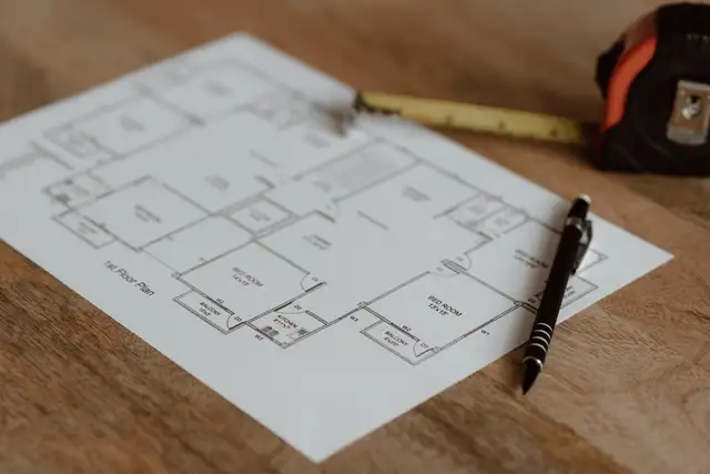 Printed floor plan on a wooden table with a tape measure and a pen